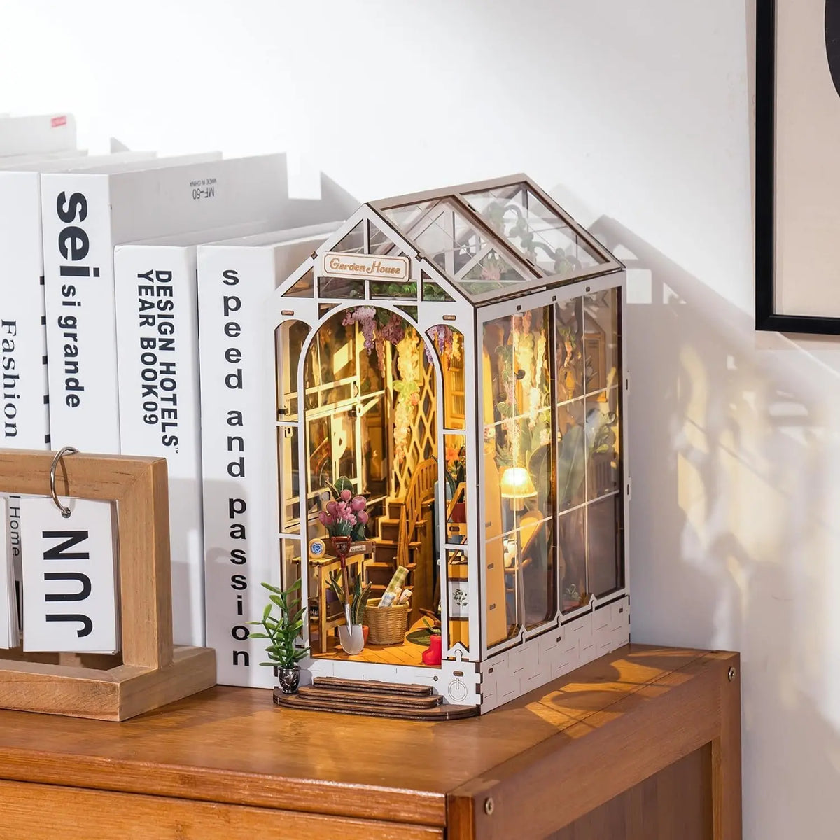 Miniature model of a glass house on a wooden surface with books in the background