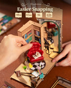 Handheld miniature bookshelf model with furniture and decorative items, labeled 'Easier Snapping' on a wooden surface.