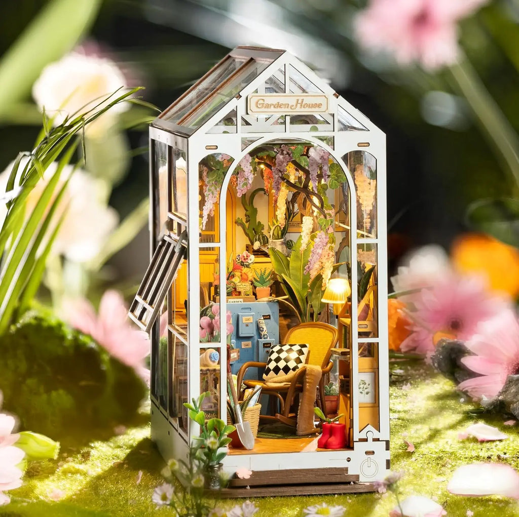 Miniature garden house model with plants and furniture on a grassy background